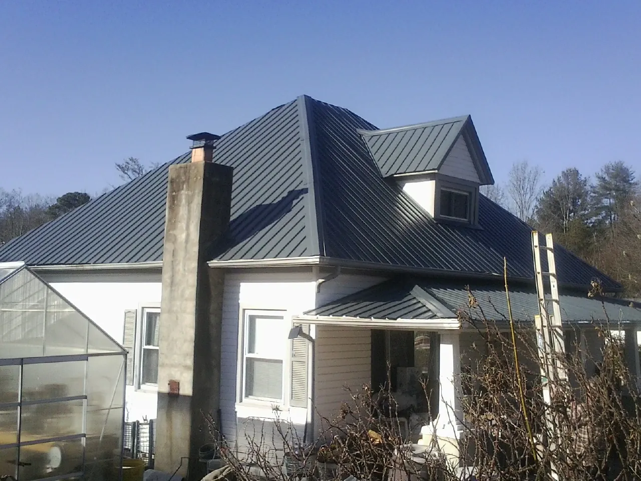 Dark blue standing seam metal roof on a white farmhouse with dormer — Slate & Tile Roof Repair by Roofing Brothers in Floral