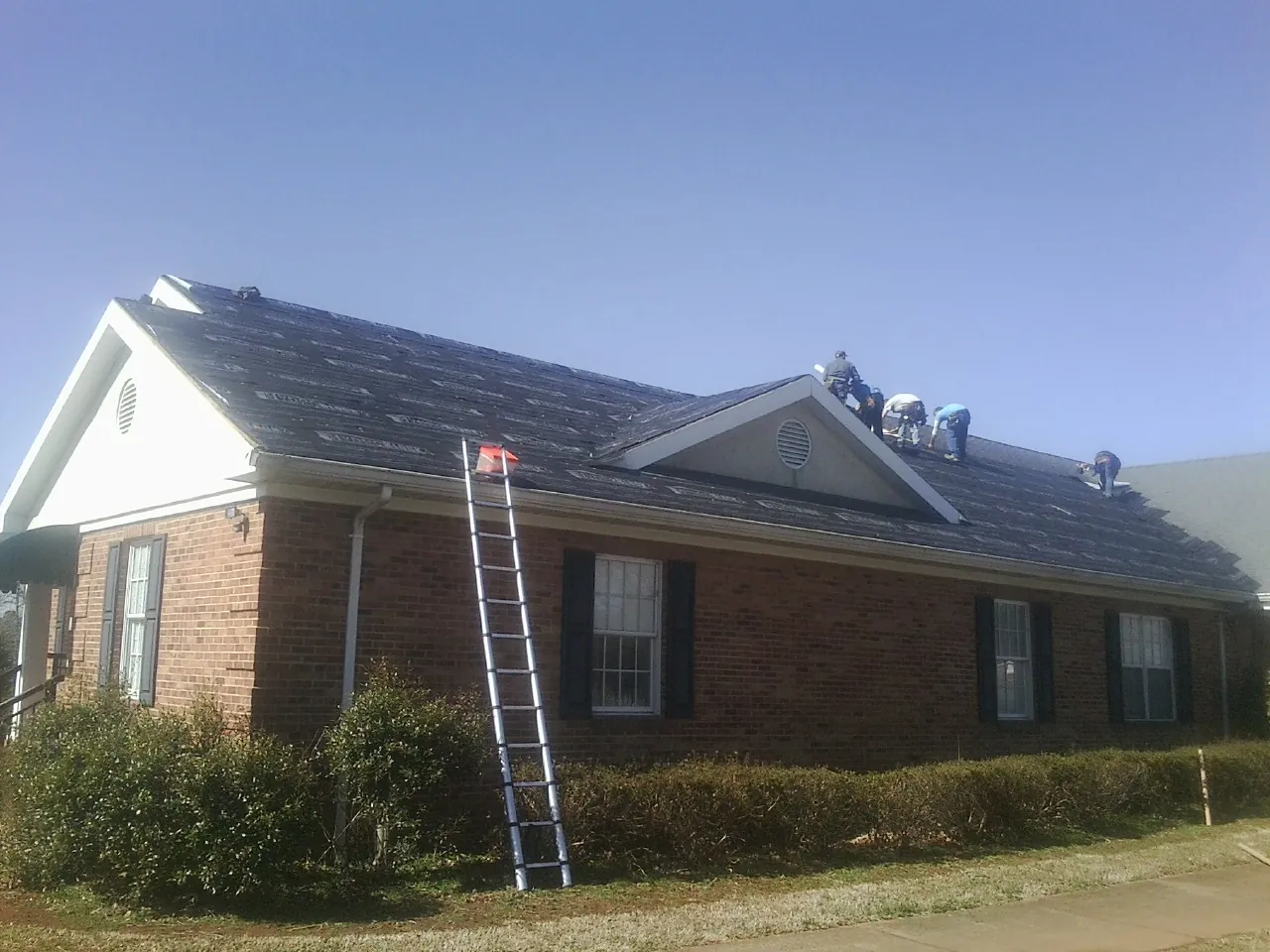 Crew tearing shingles off a brick ranch roof with a ladder set — Emergency Roof Repair work by our crew in Floral