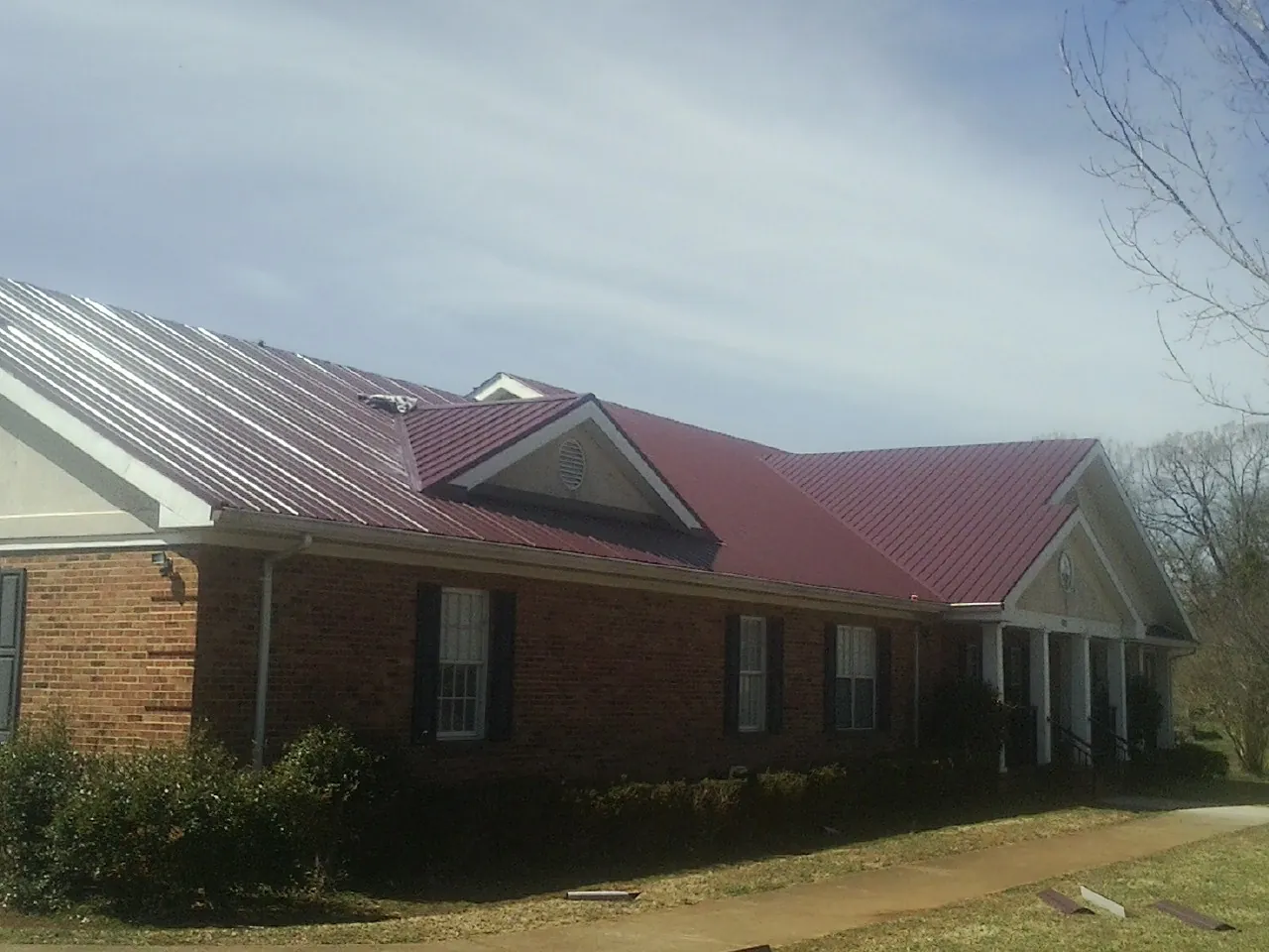 Red metal roof with gabled entries on a long brick building, from a Hail Damage Roof Repair job in Floral