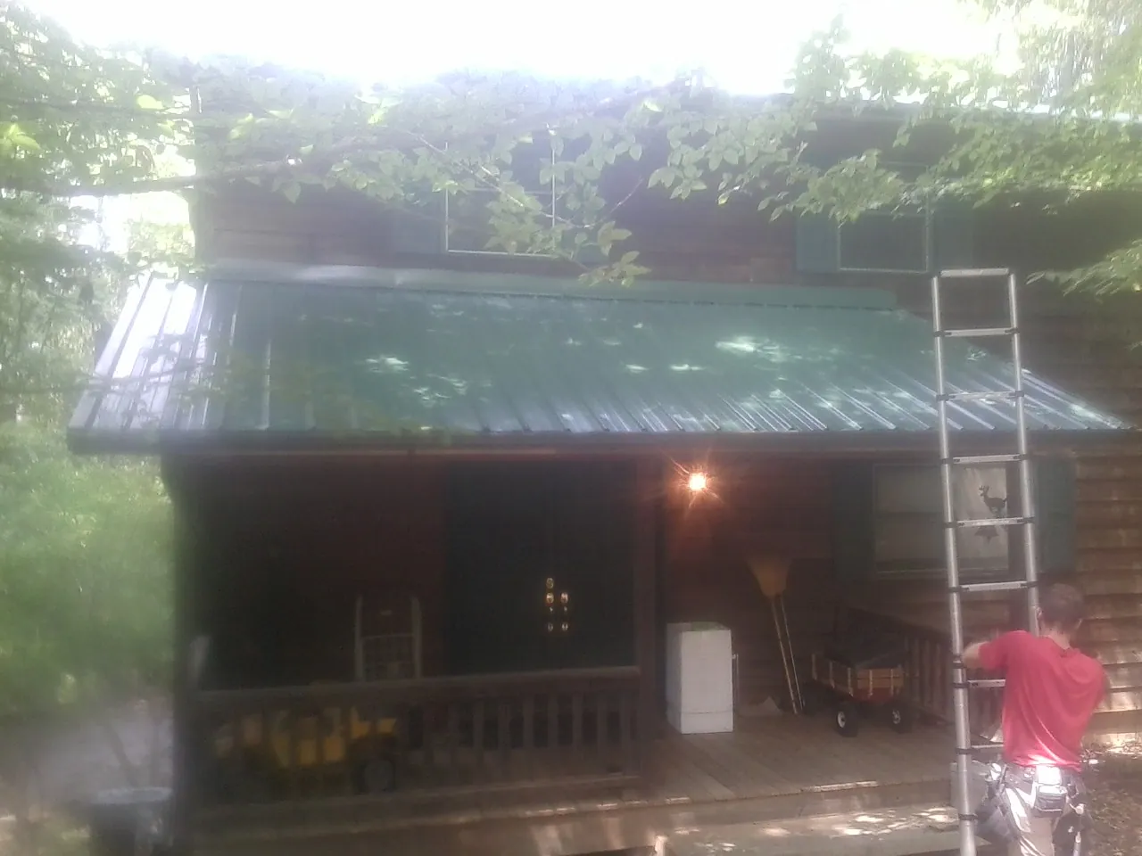 Worker on a ladder at the green porch roof of a wooded cabin in Floral