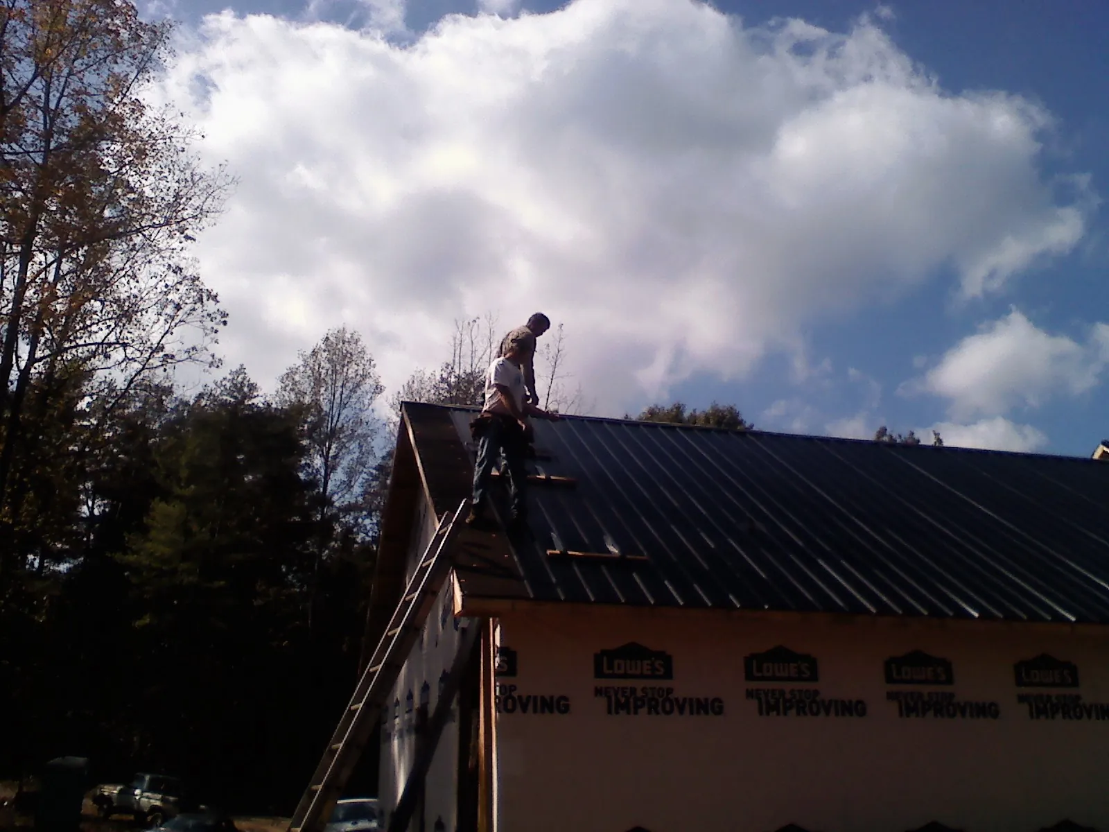 Roofer fastening dark metal panels high against a cloudy sky, from a Roof Inspection job in Floral