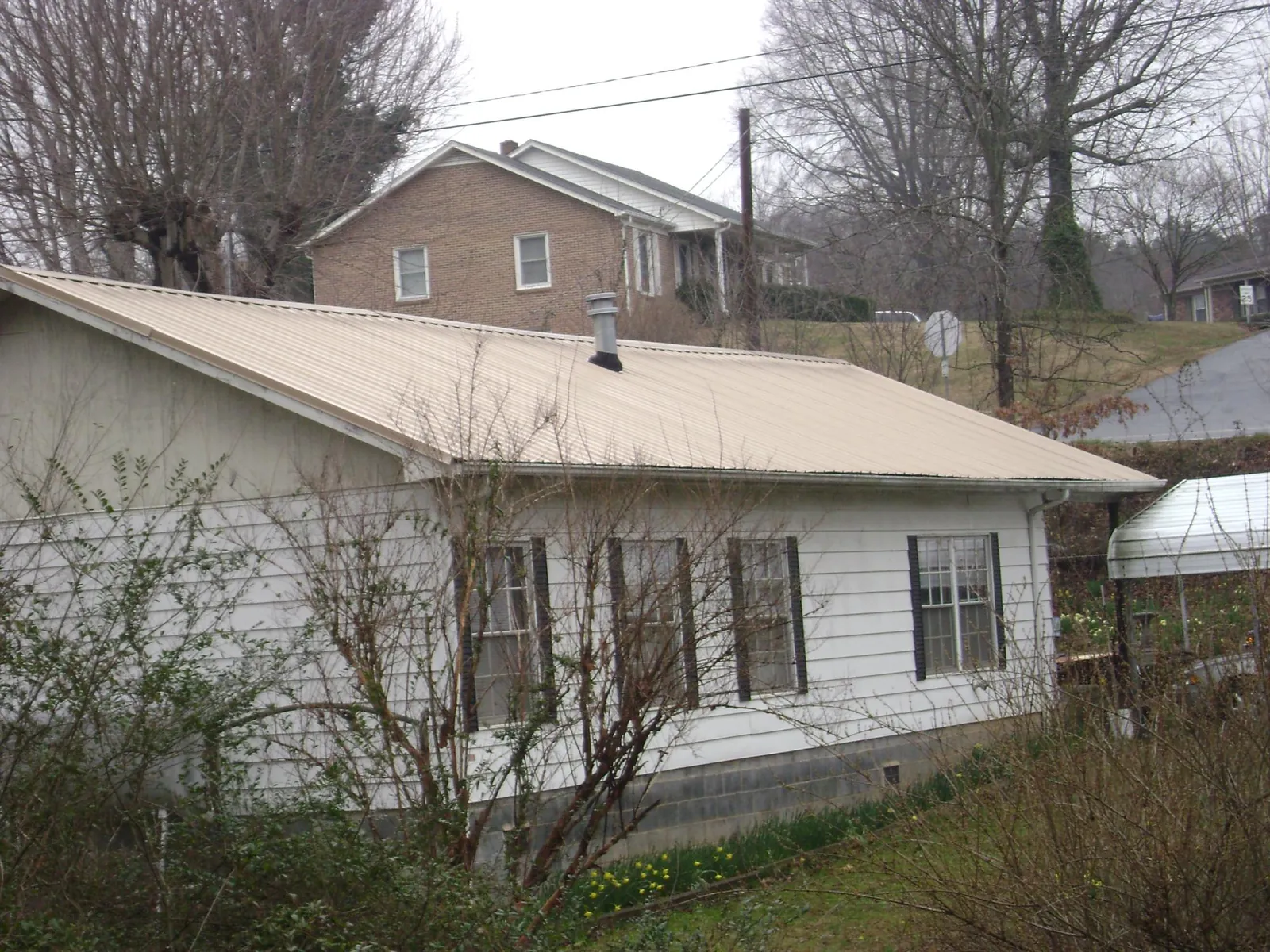 Tan metal roof on a white sided house set into a hillside — Commercial Roofing by Roofing Brothers in Floral
