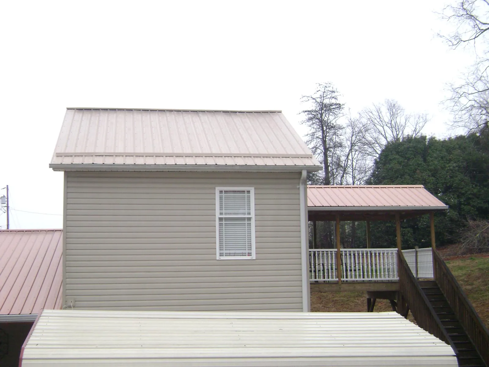 Tan metal roofs on a two story addition and attached porch, from a Roof Replacement job in Floral